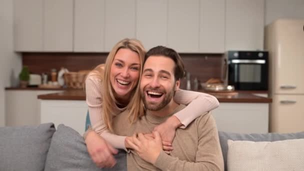 Χαρούμενο καυκάσιο ζευγάρι ερωτευμένο κάθεται στον καναπέ αγκαλιασμένο και κοιτάζει την κάμερα — Αρχείο Βίντεο