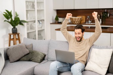 Excited caucasian businessman looking at the laptop screen and rejoicing. Happy guy screaming yes staring with mouth opened at monitor