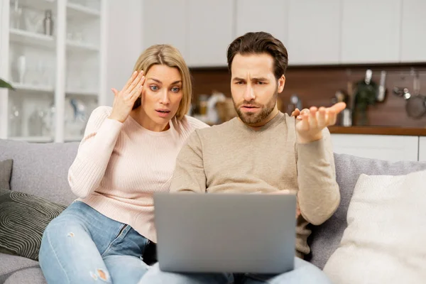 У молодой кавказской пары финансовые проблемы. Расстроенная жена и расстроенный муж просматривают счета на ноутбуке — стоковое фото