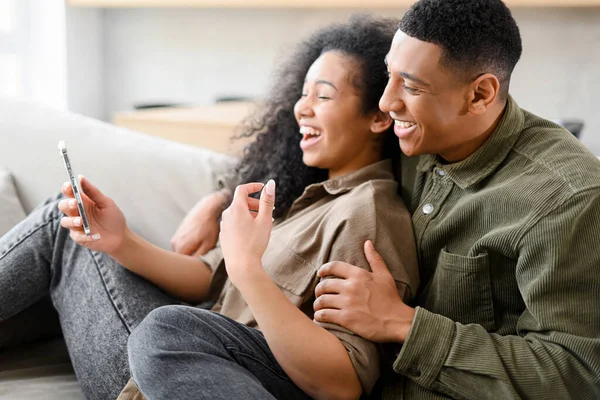 Вид збоку закоханої пари сидить на дивані вдома і використовує смартфон для розмови онлайн, відеозустріч з друзями — стокове фото