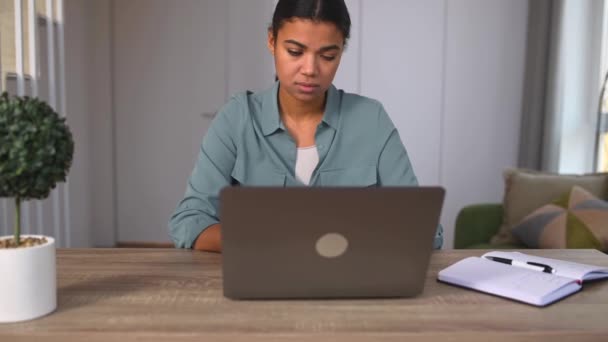 Πολυφυλετική γυναίκα ελεύθερος επαγγελματίας ή φοιτητής κάθεται στο γραφείο με φορητό υπολογιστή, αίσθημα κόπωσης — Αρχείο Βίντεο