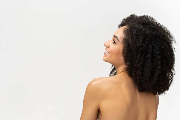 裸の肩を持つ豪華な多人種のブルネットの女性は、白の背景を見上げて笑っています。治療とケア — ストック写真