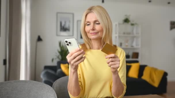 Spokojeně usměvavá zralá žena sedící na gauči a platící na internetu — Stock video