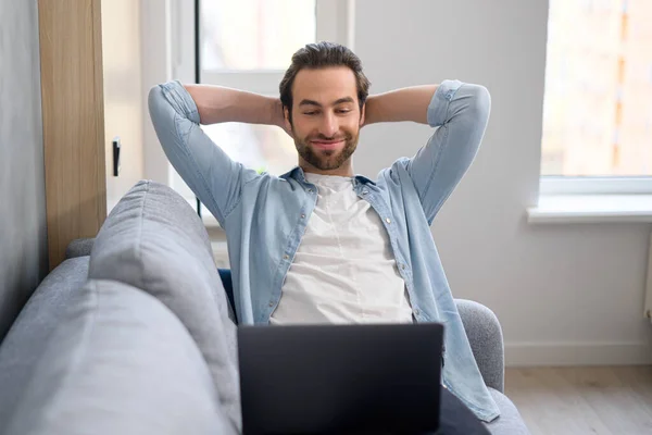 Knappe jonge Europese man met baard op de bank met laptop thuis, zoeken op het internet, kijken naar film of serie, ontmoeting op afstand, in het weekend, ontspannen — Stockfoto