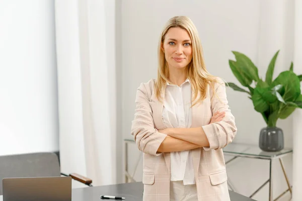 Cheerful young caucasian woman with blonde hairstyle standing in contemporary office, looking at the camera — Stockfoto
