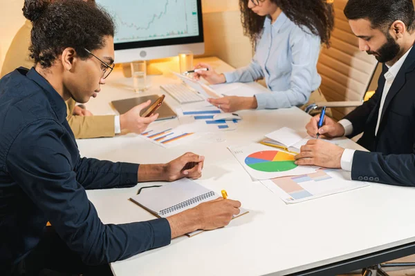 Processo di lavoro di colleghi in atmosfera seria. Persone sedute al tavolo e che scrivono alcune note mentre esaminano i diagrammi — Foto Stock