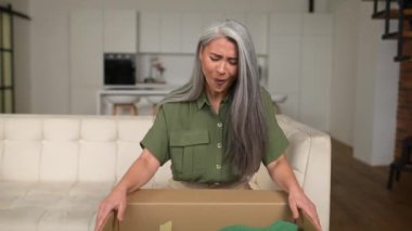 Tatmin olmuş stil sahibi son sınıf Asyalı kadın paket kutusunu açıp hediyelerini açıyor.