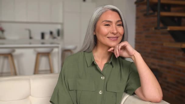 Lättsam positiv medelålders kvinna med långt grått hår sitter på soffan — Stockvideo
