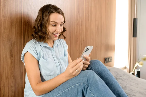 Overjoyed woman looking at phone screen, celebrating success. Excited satisfied young female holding smartphone, reading good news in message, lottery win — Stockfoto