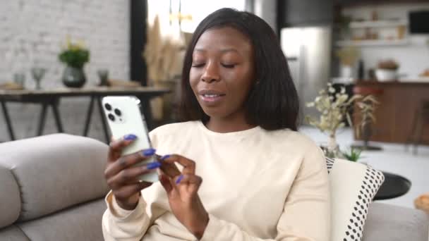 Nadšený mladá žena v ležérní oblečení se raduje sedí na gauči a drží smartphone — Stock video