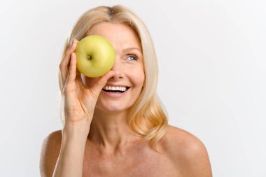 Neşeli, olgun, 50 'li yaşlarda bir gözünü taze yeşil elma kaplamış ve gülüyor.