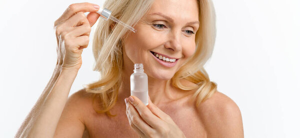 Sophisticated middle aged woman applies regenerating serum on the face