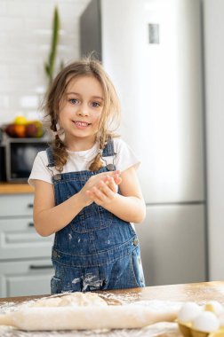 Küçük tatlı kız yemek pişiriyor ve kameraya bakıyor. Çocuk boş zamanlarını evde geçiriyor, kurabiye pişiriyor, hafta sonunun tadını çıkarıyor.
