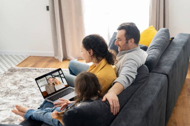 Dört kişilik aile büyükbabaları ya da aileleriyle video bağlantısı için dizüstü bilgisayar kullanıyor. Çok ırklı anne, baba ve iki çocuk dizüstü bilgisayarlarında el sallıyorlar.