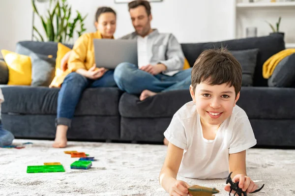两个家长坐在舒适的客厅沙发上，看着笔记本电脑，而他们的儿子则在地板上玩耍 — 图库照片