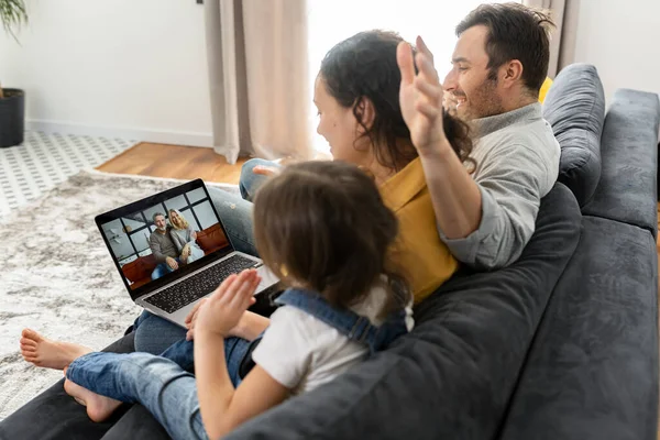 Family of four using laptop for video connection with grandparents or family. Multiracial mom, dad and two kids waving in webcam of the laptop, video call — Zdjęcie stockowe