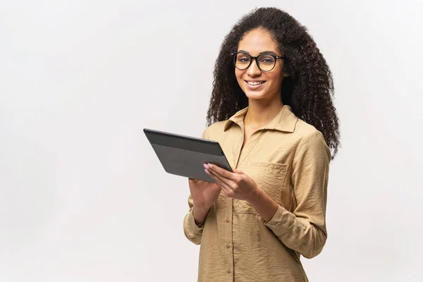 Attractive young afro american woman in glasses and smart casual shirt standing and using tablet computer — стоковое фото