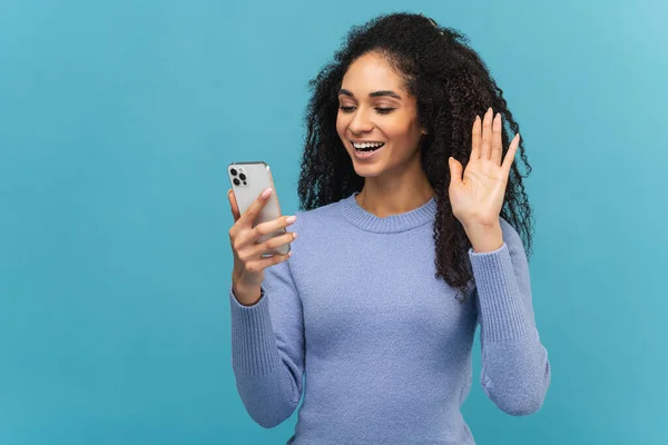 Joyful African American young woman in violet sweater using smartphone for video call — стоковое фото