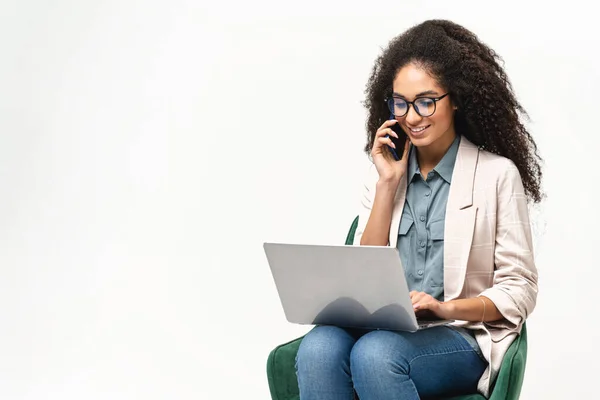 Femme afro-américaine confiante en tenue décontractée intelligente utilisant un ordinateur portable et parlant sur le smartphone — Photo