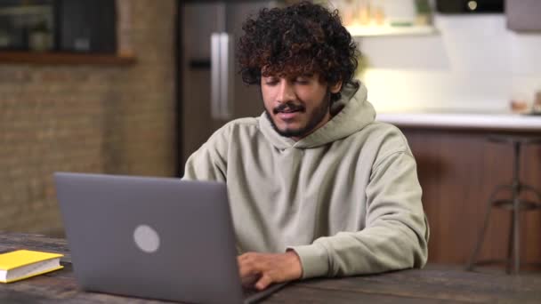 Щасливий і оптимістичний індійський чоловік у повсякденному одязі, користуючись ноутбуком у сучасній квартирі. — стокове відео
