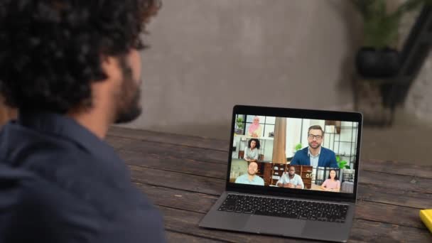 Young guy relaxed sitting at the table and talking online via video call with group — Wideo stockowe