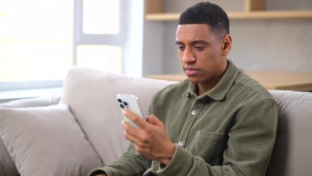 忧心忡忡的多种族千禧年男人拿着智能手机坐在沙发上 — 图库视频影像