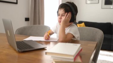 Okul çocuğu ev ödevi yapıp kulaklıkla müzik dinliyor, uzaktan ders çalışıyor.