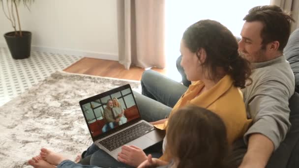 Семья из четырех человек использует ноутбук для видеосвязи с бабушкой и дедушкой или семьей — стоковое видео