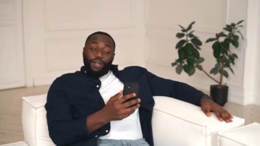 Heyecanlı Afro-Amerikalı adam elinde cep telefonu tutuyor ve internetteki interneti selamlıyor.