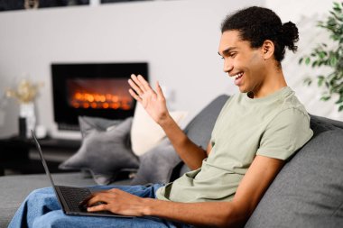 Video iletişimi, yakınlaştır. Çok ırklı bir gencin evdeki video görüşmesi için dizüstü bilgisayar kullanırken el sallıyor.