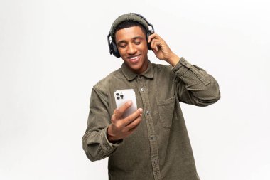 Sevinçli, neşeli, çok ırklı adam favori şarkıları dinliyor, beyazda izole edilmiş. Telsiz kulaklık takan neşeli latin adam elinde akıllı telefon tutuyor.