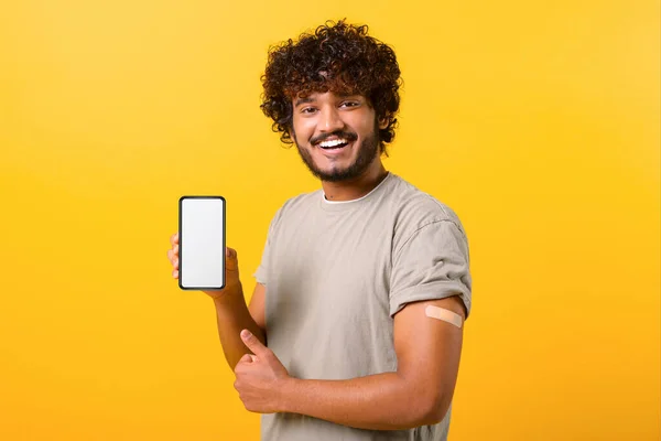 Χαμογελώντας σγουρά ινδική άνθρωπος με ιατρική ταινία-ενίσχυση στο χέρι n δείχνει smartphone — Φωτογραφία Αρχείου