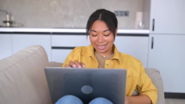 Avslappnad ung afro-amerikansk kvinnlig frilansare sitter på soffan titta på film — Stockvideo
