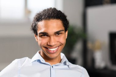 Tatmin olmuş genç adam rahat bir kanepede dinleniyor modern oturma odasında, dişlek bir gülümsemeyle kameraya bakıyor.