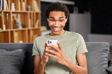 Akıllı telefondan mesaj gönderen yakışıklı bir adam, rahat koltukta oturuyor, elinde cep telefonu, mesaj atıyor.