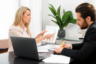 Takım çalışması. Genç adam ve kadın ellerindeki belgeye bakıyor ve bir şeyi tartışıyorlar.