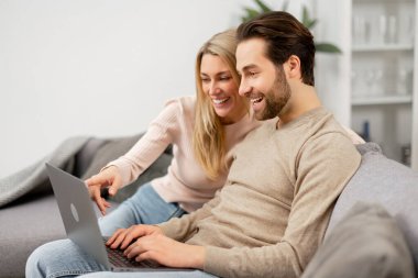 Kafkasyalı aşık çift evde dizüstü bilgisayarla vakit geçiriyor. Mutlu kız arkadaş ve erkek arkadaşı kanepede otururken dizüstü bilgisayara bakıyorlar.