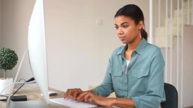 Motive olmuş genç bir kadın ofis masasında oturmuş web sörfü için bilgisayar kullanıyor.