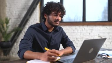 Zeki Hintli işadamı, modern ofiste otururken bilgisayardaki sanal toplantıya dahil oldu.