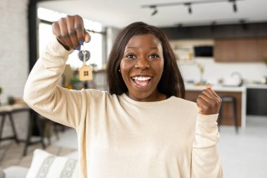 Happy young woman holds key of new home, looks at the camera and screams ecstatic, amazed girl celebrates relocation in own apartment, buying a property