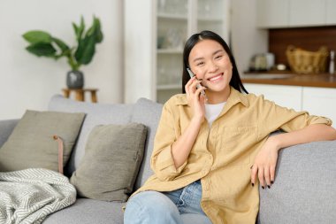 Gülümseyen genç bir kadın cep telefonuyla arkadaşlarıyla sohbet ediyor, keyifli telefon konuşmaları yapıyor.