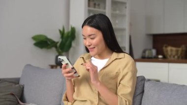 Yakışıklı Asyalı kadın elindeki akıllı telefona bakıyor.