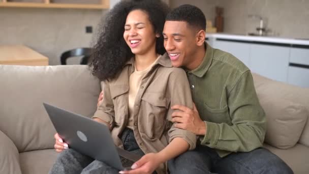 Χαρά πολυφυλετικό ζευγάρι στην αγάπη ξοδεύοντας ελεύθερο χρόνο σε απευθείας σύνδεση με ένα φορητό υπολογιστή στο σπίτι — Αρχείο Βίντεο