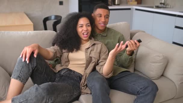 Νεαρό Αφροαμερικανό ζευγάρι ερωτευμένο να κάθεται στον καναπέ και να βλέπει τηλεόραση — Αρχείο Βίντεο