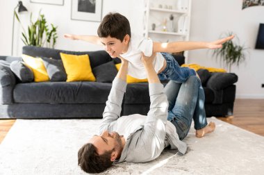 Sevgili baba, Sonny ile oynuyor. Mutlu baba ve okul çağındaki oğlu evde birlikte vakit geçiriyorlar, rahat oturma odasında yerde uzanıyorlar, baba çocuğu taşıyor.