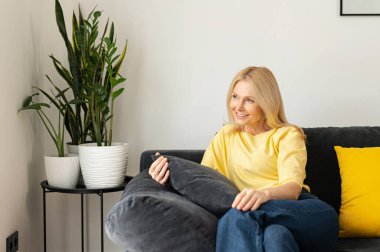 Kaygısız beyaz kadın kanepede oturuyor ve dinleniyor. Çekici sarışın kadın portresi hayal kuruyor