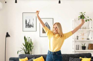 Çekici, olgun, orta yaşlı iş kadını gülümseyen, modern evde oturan, sarı kazak giyen.