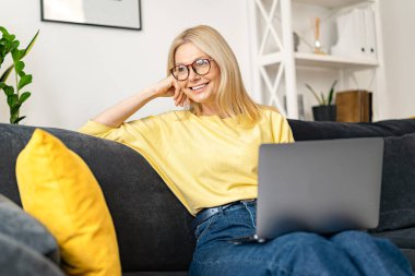 Senior caucasian female businesswoman or female freelancer in comfy casual clothes sitting on the couch and working on the project