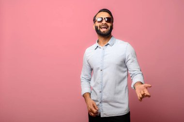 Güneş gözlüklü neşeli Hintli adam gitarist rolü yapıyor.