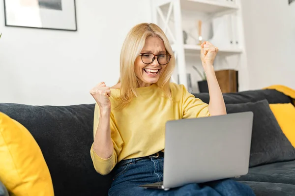 Heureux heureux milieu des années 60 femme mûre dans les lunettes de vue regardant l'écran d'ordinateur portable, lire l'email avec des nouvelles étonnantes, célébrer la victoire de loterie en ligne — Photo